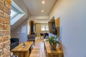 Ein Loft-Wohnraum mit hoher Decke, Dachfenster, einem Essbereich mit Tisch und Stühlen, einer Couch und einem an der Wand befestigten Fernseher.