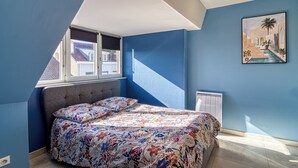 A bedroom with a bed, a window, a radiator, and a painting on the wall. - 2-bedroom apartment "Le Chaleureux (Dunkerque)