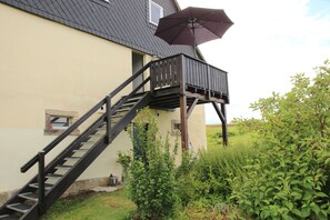 A house with a wooden staircase leading to a balcony, surrounded by greenery. - Holiday Apartment for 3 Guests (45 m²) in Bertsdorf-Hörnitz (Bertsdorf-Hörnitz)