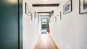 Käytävän lattia on parkettia, seinillä on kehystettyjä tauluja, katossa on kattovalaisin ja seinällä palosammutin.