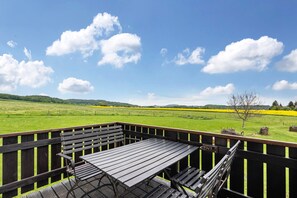 Um deck de madeira com mesa e bancos, com vista para um campo verde e colinas.
