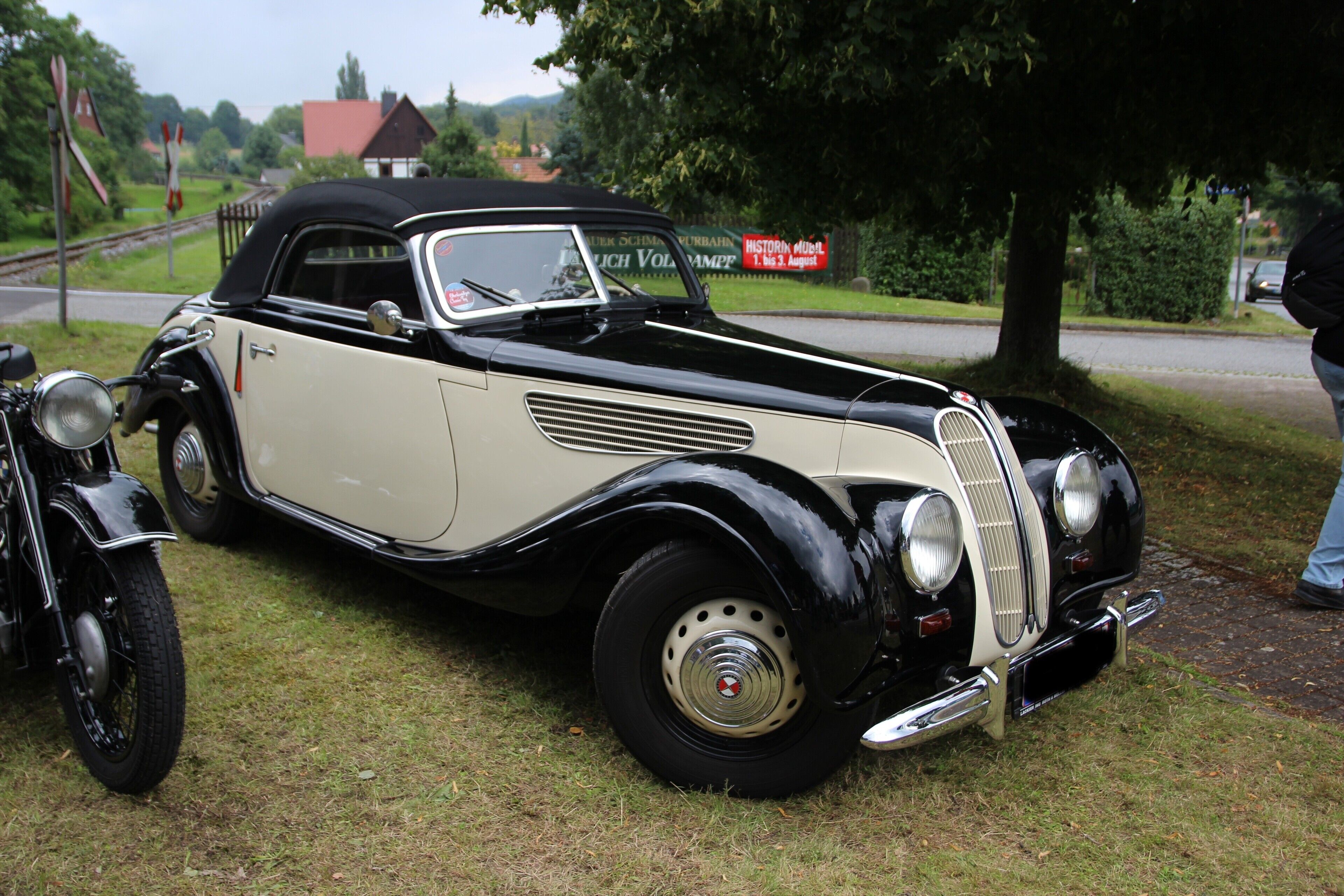 Een oldtimer geparkeerd op gras met een motorfiets ernaast.