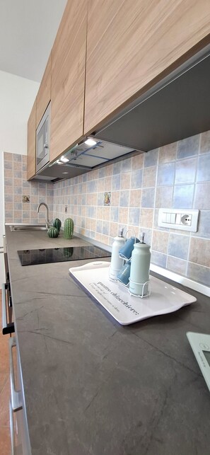 A kitchen with a modern design, featuring wooden cabinets, a stainless steel range hood, a tiled backsplash, and a countertop with a built-in stove. - La Dolce Vita - Key to Villas (Valledoria)