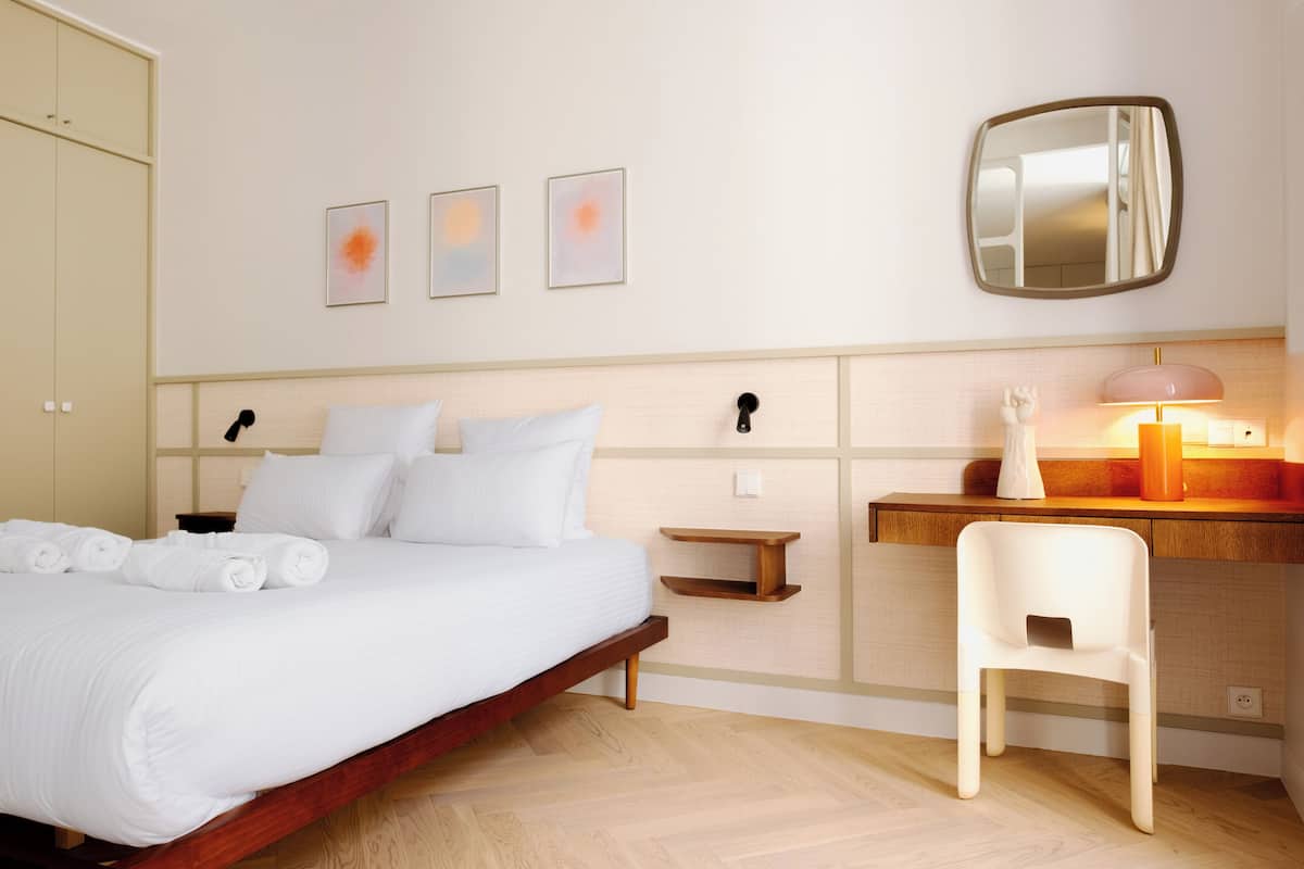 A hotel room with a bed, bedside table, chair, and a mirror.