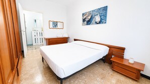 Une chambre à coucher avec un lit, des tables de chevet en bois, un tableau et une porte donnant sur une autre pièce.