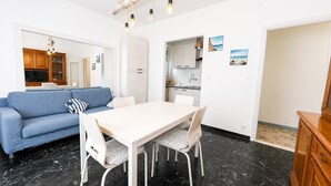 Un salon moderne comprenant un canapé, une table à manger et des chaises, un coin cuisine avec des placards, et une vue sur la mer.