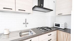 Une cuisine moderne avec des meubles blancs, un évier en acier inoxydable, une cuisinière à gaz et un four à micro-ondes blanc.