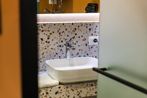 Ein Badezimmer mit einem weißen Waschbecken, einem Spiegel und einer Wand mit Terrazzo-Muster.