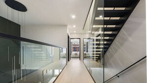 Un interno moderno con ringhiera in vetro, una scala e vista su una stanza con un letto.