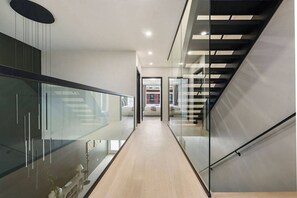 A modern interior with a glass railing, a staircase, and a view into a room with a bed. - Rooftop Sauna + Hot Tub | Spa Room | Cabana! (Pittsburgh)