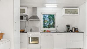 Una cocina moderna con armarios blancos, horno empotrado, microondas y ventana con vista a árboles.