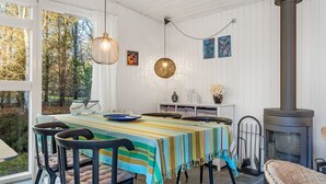Un comedor con una mesa lista para cuatro personas, una lámpara colgante y un estufa de leña.