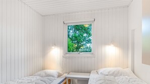 Un dormitorio con dos camas individuales, una ventana con vistas a árboles y una pared blanca con una lámpara.