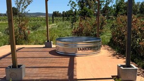 A metal tank with 'TANKKD' and 'A WATERTING CISTER' text, surrounded by a wooden pergola structure in a landscaped outdoor setting.