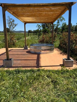 Un réservoir métallique portant les inscriptions « TANKKD » et « A WATERTING CISTER », entouré d’une structure en pergola en bois, dans un espace extérieur aménagé.