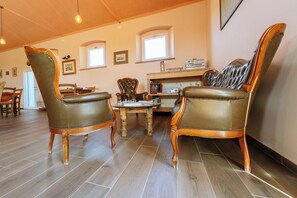 A spacious living room with wooden flooring, leather armchairs, a wooden coffee table, and a bookshelf with various items. - Podere 109-BioWine: Exclusive Villa with Hot Tub in the Tuscan Maremma (Toscana)