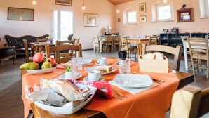 A dining area with tables set for breakfast, featuring fruits, bread, and beverages.