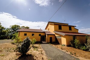Une maison jaune à deux étages, avec un toit en tuiles, une allée gravillonnée et un petit jardin.