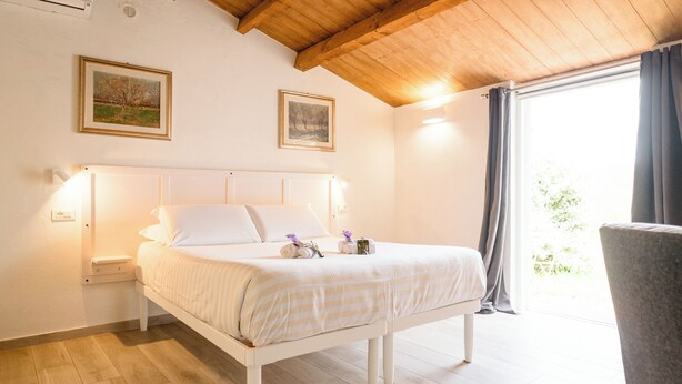 A bedroom with a wooden ceiling, a bed with white bedding, two wall-mounted lamps, and a window with curtains.