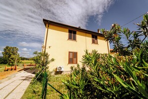 A two-story building with a yellow facade, brown shutters, and a visible air conditioning unit. - Podere 109-BioWine: Exclusive Villa with Hot Tub in the Tuscan Maremma (Toscana)