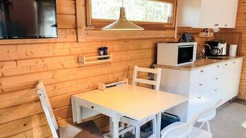 Una cocina compacta con una mesa blanca, sillas, un microondas y un televisor montado en la pared.