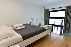 Ein modernes Schlafzimmer mit Bett, Kissen, einem Fenster mit Vorhängen und einem Balkon.