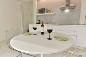 Eine moderne Küche mit einem weißen Tisch, zwei Weingläsern, einer Weinflasche und einer Mikrowelle auf der Arbeitsplatte.