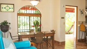Un comedor con mesa de madera, sillas de mimbre y ventana con vista a la vegetación.