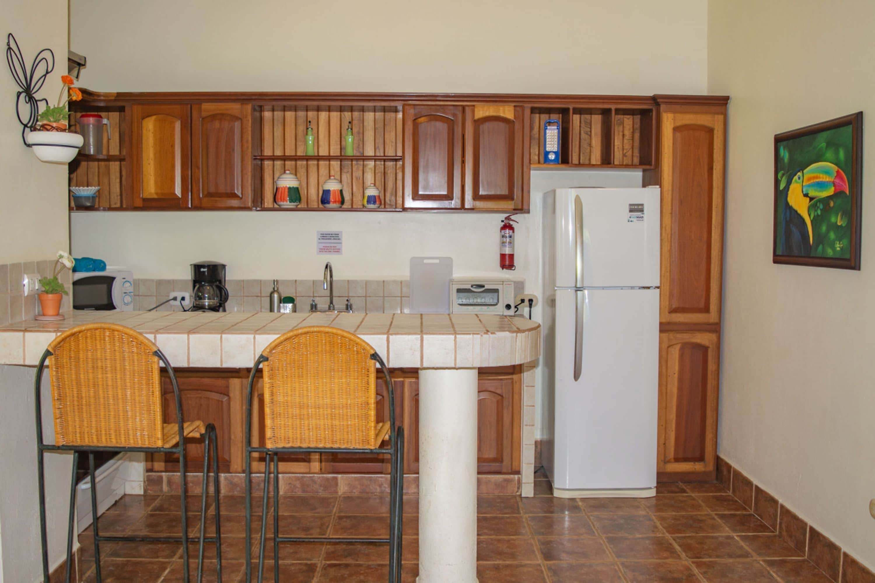 Eine Küche mit Holzausstattung, einem weißen Kühlschrank, zwei Korbstühlen und einer gefliesten Spritzschutzwand.