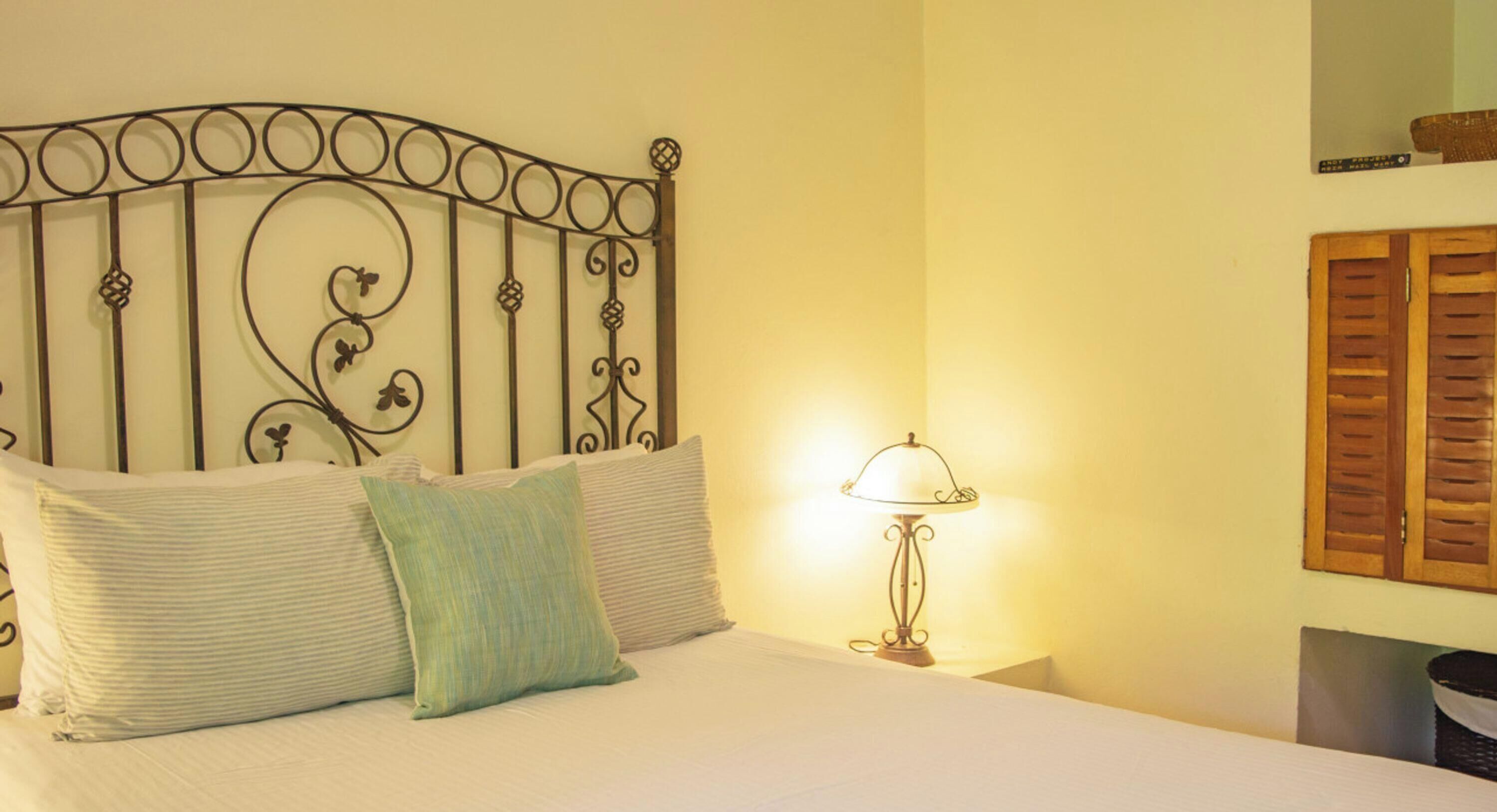 Ein Bett mit Metallkopfteil, einer Lampe und einem Holzklappladen an der Wand.