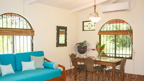 Habitación con sofá de madera, mesa de comedor, sillas, lámpara colgante y ventana con reja de metal.