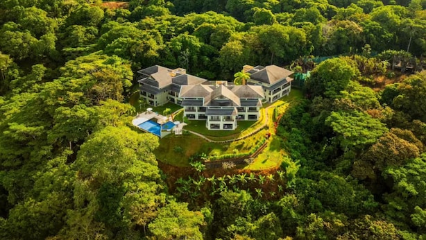 A large, multi-story building surrounded by dense greenery, with a swimming pool and a well-maintained lawn. - Condo With Stunning Beach and Wildlife Views (Bahía Ballena)