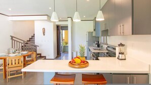 A modern kitchen with a central island, a dining area with wooden furniture, and a staircase leading to another level. - Condo With Stunning Beach and Wildlife Views (Bahía Ballena)