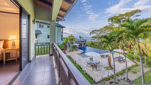 A balcony with a view of a pool, palm trees, and a building with a tiled floor. - Condo With Stunning Beach and Wildlife Views (Bahía Ballena)