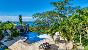 A pool area with a view of the ocean, surrounded by palm trees and a modern building. - Condo With Stunning Beach and Wildlife Views (Bahía Ballena)