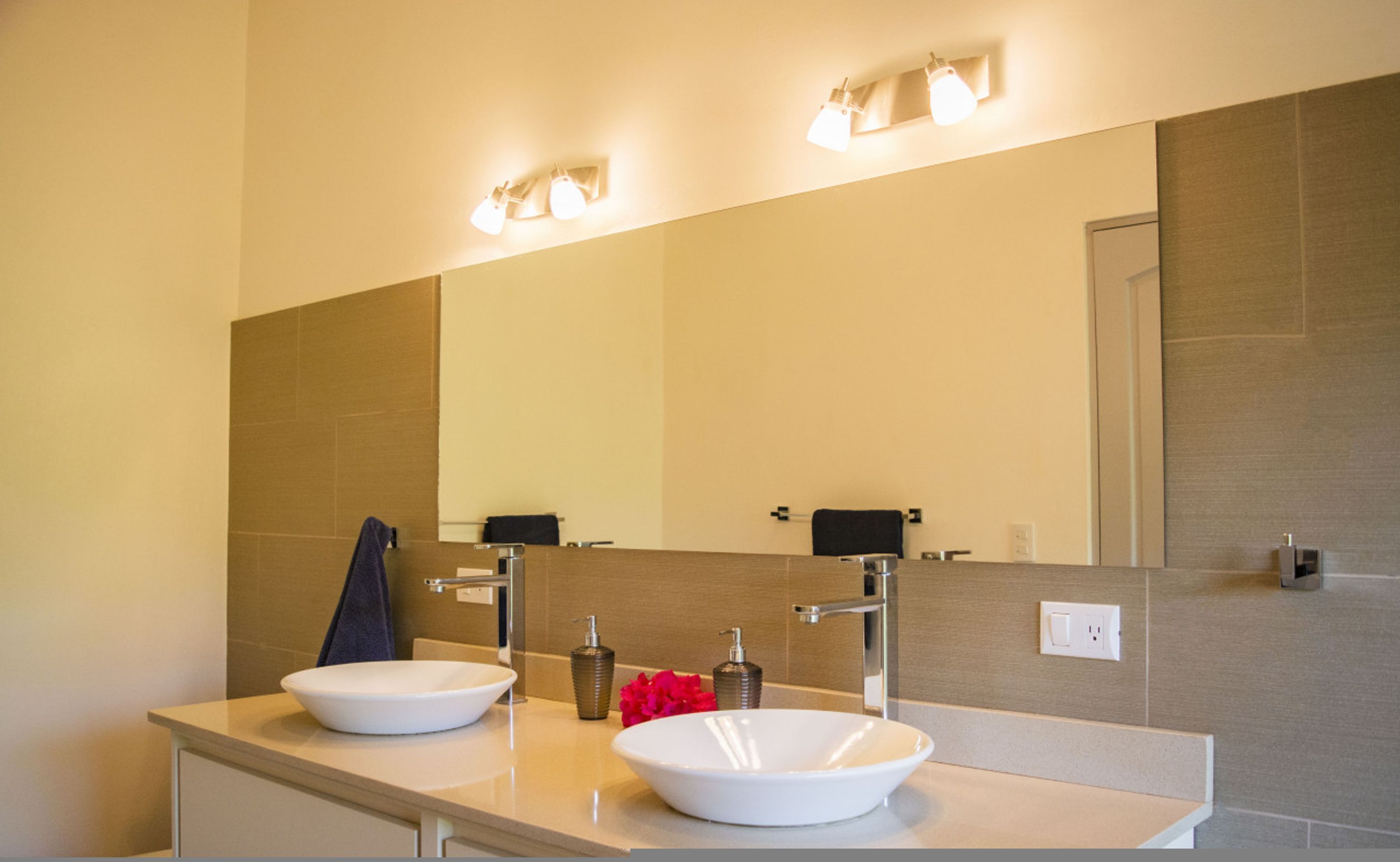 A modern bathroom with two sinks, a large mirror, and wall-mounted lights.