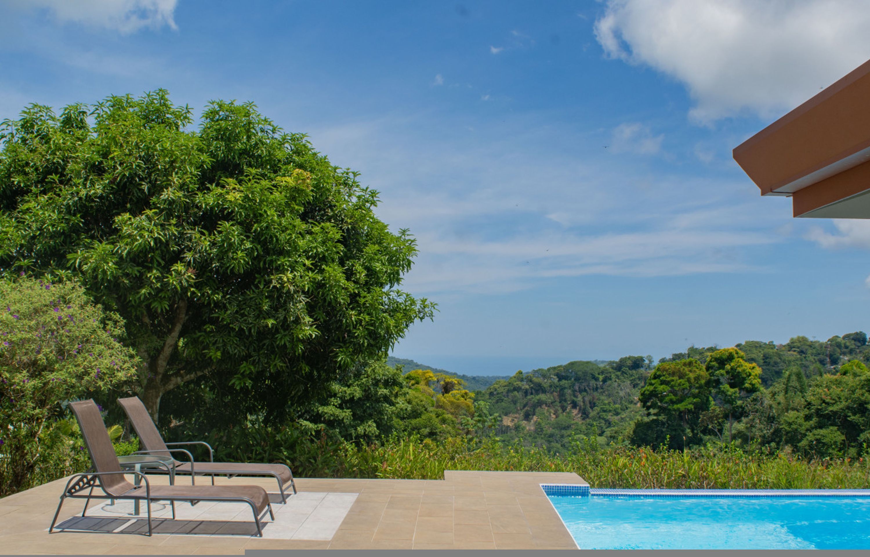 A pool with two lounge chairs, a tiled deck, and a view of a forested hillside.