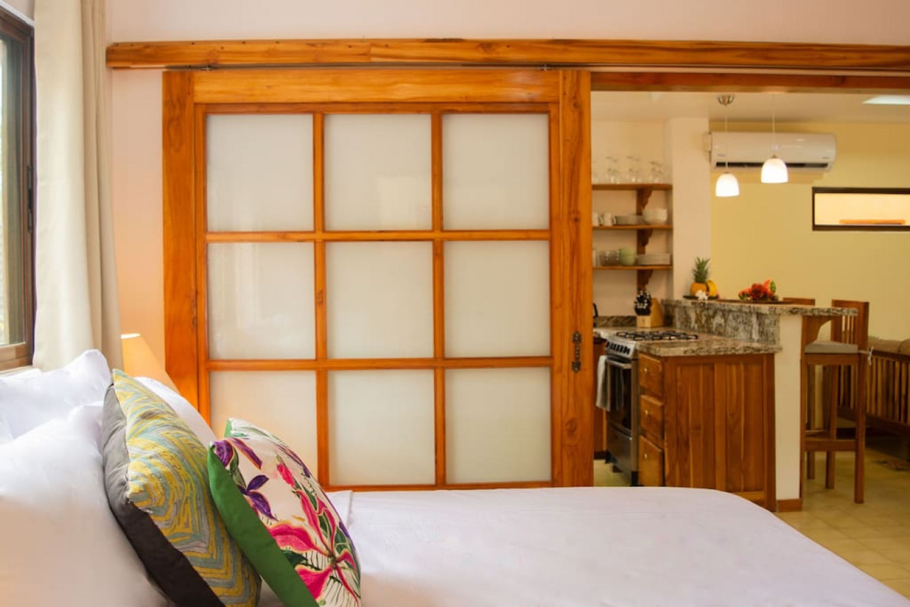 Une chambre avec un grand lit, une porte coulissante à cadre en bois et un coin cuisine comprenant une table et des chaises.