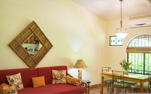 A living room with a red sofa, a dining table, a lamp, and a decorative mirror.