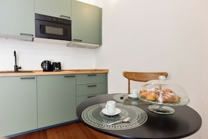 A kitchen with a microwave, coffee maker, and a table with a glass dome displaying pastries. - 4BNB - Loft Colosseum 1 (Rome)