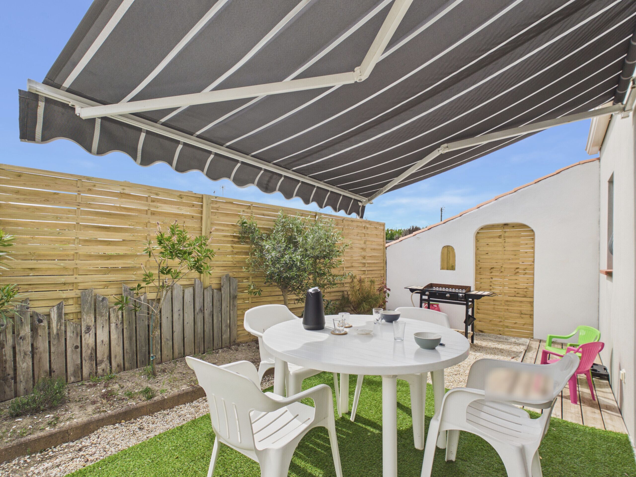 A patio with a round table, white chairs, a grill, and a wooden fence.