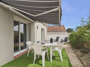 Un patio con mesa y sillas, una zona cubierta y vistas a un edificio cercano.