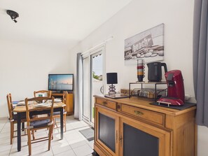 Una habitación con una mesa de comedor, sillas, televisor, cafetera y un armario.