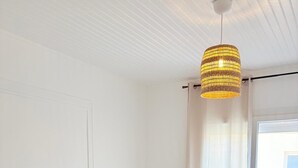 Ett modernt sovrum med en stor säng, en mindre säng, en hängande lampa och ett fönster med gardiner.