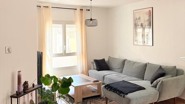 Ett vardagsrum med en soffa, ett soffbord och en hängande lampa.
