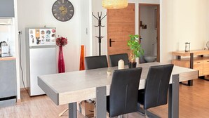 Ett modernt matområde med ett långt bord, svarta stolar, en hängande lampa, en klocka och ett kylskåp med magneter.