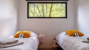 A bedroom with two beds, a window with a view of trees, a pink lamp, and a wooden nightstand.