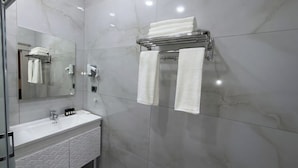 Un baño moderno con pared de mármol, cabina de ducha de vidrio, lavamanos blanco con salpicadero geométrico y toallero con dos toallas.