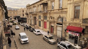 Una calle empedrada flanqueada por edificios históricos, coches aparcados y peatones.