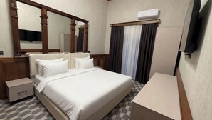 Habitación de hotel con cama, mesitas de noche, espejo, armario, televisión de pantalla plana y equipo de aire acondicionado.